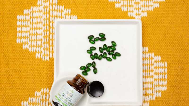 CBD oil capsules in a bottle on a white tray over an orange patterned fabric. Ideal for health and wellness themes., tags: markt für cbd-gelkapseln bis 2032 - pexel