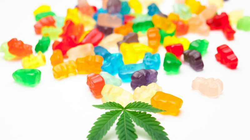 Vibrant gummy bears scattered alongside a cannabis leaf on a white background., tags: cbd-gummis und - pexel